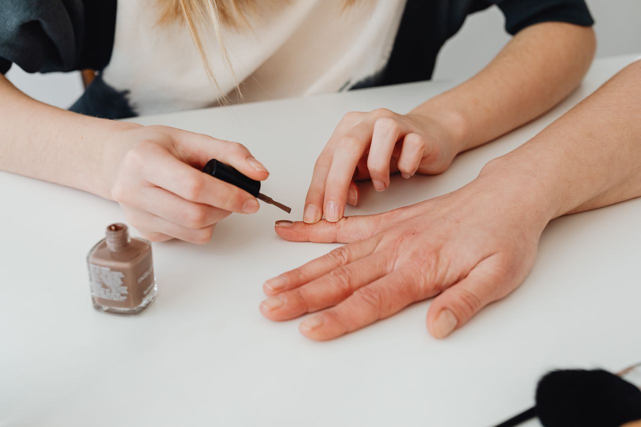 Close-up of hands during a manicure session, applying nail polish in a salon setting.